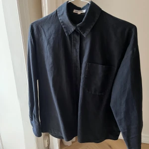 Svart skjorta från Djerf Avenue - Klassisk svart skjorta från Djerf Avenue i storlek XS. Skjortan har lång ärm, bröstficka och knäppning framtill. Perfekt för en stilren och enkel look. Gjord i mjukt bomullstyg och har en rak passform.