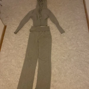  set - Säljer en beige stickad hoodie med långa ärmar och huva. Tröjan är ribbad och har en croppad passform, perfekt för en avslappnad stil. Matchande byxor ingår ej i annonsen.