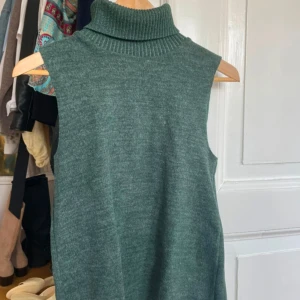 Grön ärmlös polotopp från Zara - Säljer en stickad grön ärmlös polotopp från Zara. Perfekt att styla med skjorta under eller som den är. Mjuk och skön med hög polokrage. Passar dig som gillar en enkel men trendig look.