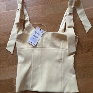 Ljusgul linnetopp med knytband - Supersöt ljusgul linnetopp med breda axelband som knyts upptill. Toppen har en rak, croppad passform och är perfekt för varma dagar. Stilren och enkel design som passar till mycket.