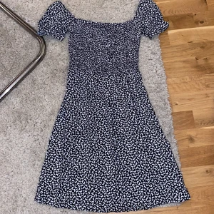 Svart klänning med fjärilsmönster från B Sister - Supersöt svart klänning från B Sister med vita fjärilar över hela tyget. Klänningen har korta puffärmar, smockad överdel och knytband i ryggen. Perfekt för varma dagar och ger en lekfull vibe till din outfit.