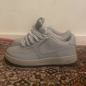 Nike Air Force 1 i ljusgrått - Säljer ett par klassiska Nike Air Force 1 i ljusgrå färg. Skorna har en låg siluett, rund tå och snörning. Ovandelen är i skinn med diskreta sömmar och Nike-logga på sidan samt AIR-detalj på sulan. Perfekta för dig som gillar stilrena sneakers.