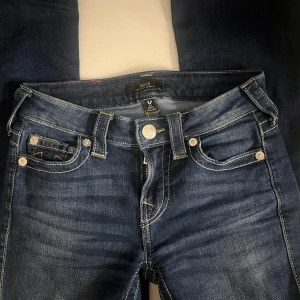 Mörkblå jeans från True Religion - Säljer ett par klassiska mörkblå jeans från True Religion med kontrastsömmar och ikoniska bakfickor. Byxorna har normal passform, låg midja och silverfärgade knappar. Perfekta för dig som gillar streetwear och snygga detaljer. Säljer dem då dem inte passar mig dem är helt oandvända bara andvänder en gång då jag testade dem.💞