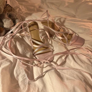 Sandalklakar med band - Säljer ett par ljusrosa sandal-klakar med långa snören som knyts runt benen. Endast testade ett par gånger då jag trode problemet var min ovana med klakar men bandet över tåboxen är något för tight över för mig. Passar för dig med smala till normala breda fötter.