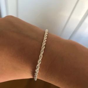 Flätat silverarmband - Säljer ett stilrent armband i silverfärg med flätad design. Perfekt för dig som gillar enkla men snygga accessoarer. Passar till många olika stilar och är lätt att matcha med andra smycken. Den är 20 cm lång 