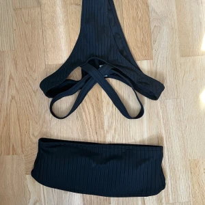 Svart ribbad bikini - Säljer en svart ribbad bikini i bandeau-modell med matchande trosor. Bikinin har en stilren design och är perfekt för stranden eller poolen. Materialet är stretchigt och bekvämt.