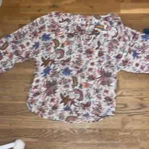 Blommig blus  - Säljer en luftig blus med blommigt mönster i rosa, blått och brunt. Skjortan har lång ärm och rundad nederkant, perfekt för en färgglad look. Passar dig som gillar bohemisk stil! Inga defekter. Använd köp nu knappen!