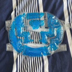 Gel bead face mask helt ny - Säljer en ansiktsmask med blå gelékulor som kan användas varm eller kall. Masken har öppningar för ögon, näsa och mun och fästs med kardborreband. Perfekt för att fräscha upp huden eller minska svullnad.