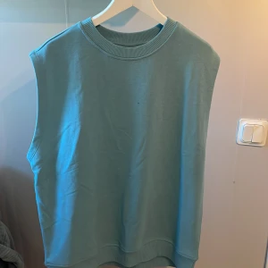 Ljusblå väst från Lager 157 - Säljer en ljusblå väst från 157 i storlek M. Västen har ribbad halsringning och nederkant, och är ärmlös med en avslappnad passform. Perfekt att styla över en skjorta eller t-shirt.