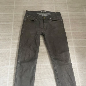 Grå jeansbyxor från Acne - Säljer ett par grå jeansbyxor från Acne i modellen Nelson Khaki. Byxorna har klassisk femficksdesign, knapp och dragkedja i gylfen samt raka ben. Materialet är 98% bomull och 2% elastan för lite stretch.