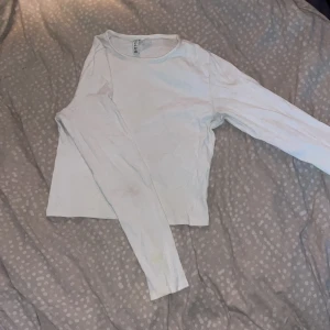 Vit ribbad långärmad topp från H&M Divided - Säljer en vit ribbad långärmad topp från H&M Divided. Toppen har en enkel och klassisk design med rund halsringning och är tillverkad i ett mjukt material som passar perfekt till vardags. Modellen är kort och tajt och slutar ungefär vid naveln. Storlek M men skulle säga att den sitter som en S. Finns en liten fläck på ena sidan av tröjan som tyvärr inte går bort i tvätten (syns på bilden), går säkert bort om man anstränger sig lite.