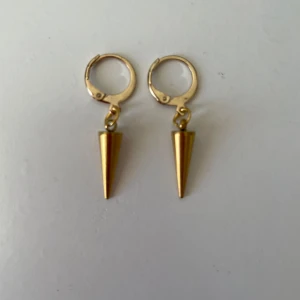 Guldiga örhängen med konformad hängande detalj - Säljer ett par handgjorda guldörhängen. Rostfritt material och nickelfria.