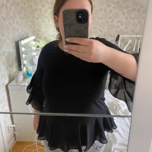 Svart blus med volang från Vero Moda - Säljer en svart blus från Vero Moda med volang nertill och vid ärmslut. Blusen har trekvartsärmar i ett lätt och luftigt material som ger en snygg och flowy look.