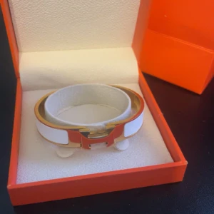 Vitt armband med gulddetaljer - Säljer ett stilrent armband i vitt med guldfärgade kanter och klassiskt H-spänne. Kommer i originalask och passar perfekt för dig som gillar lyxiga accessoarer.