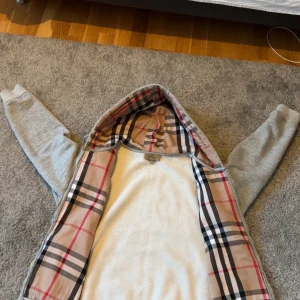Grå Burberry zip hoodie - Säljer en Burrbery kofta i storlek L perfekt för sommaren fester eller vid speciella tillfällen. Koftan är hyfsat ny använd ett par gånger men är som ny. Skriv vid flera funderingar 