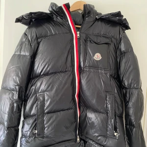 Moncler jacka - Tjaa säljer min as snygga moncler jacka pågrund av att sommaren är påväg. Jackan är äkta och finns qr kod på sista bilden. Jackan är i jättebra skick för den knappt blivit använd men det ändå problemet är att själva grejen man hänger upp jackan på är lös men för den som kan sy är de hur lätt som helst att lösa. Skicka ifall de skulle vara minsta funderingen!