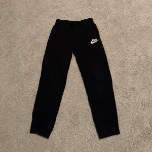 Svarta mjukisbyxor från Nike - Svarta mjukisbyxor från Nike med vit logga på vänster ben. Byxorna har resår i midjan samt två fickor💗