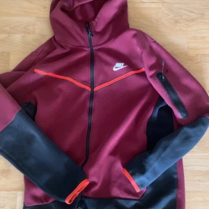 Nike tech old season vinröd  - Säljer en vinröd Nike  techmed svarta ärmar och detaljer i rött storlek L!  Dragkedjans topp har gått av så det ser så där ut. Annars riktigt bra, inte så använd. Pris går såklart att diskutera. Hör av er vid frågor!