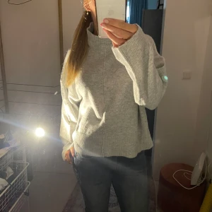 Ljusgrå stickad polotröja - Mysig ljusgrå stickad polotröja med hög krage och avslappnad passform. Tröjan har långa ärmar och en rak, något boxig siluett. Perfekt för lager-på-lager och chill dagar. Enkel att matcha med jeans eller kjol.