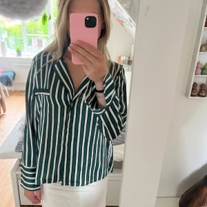 Randig skjorta från Gina Tricot - Snygg skjorta från Gina Tricot i grönt och vitt med vertikala ränder. Skjortan har klassisk krage, bröstficka och långa ärmar. Passformen är loose och materialet känns mjukt och lätt, perfekt för en chill och trendig look.