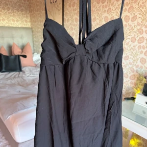 Svart kort klänning med rosett - Supersöt svart kort klänning med smala axelband och en stor rosett framtill. Klämminge är liten i brösten så passar S med! Aldrig använd då den är för liten!