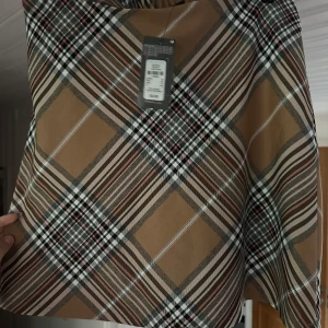 Rutig kortkjol från Primark - Superfin rutig kortkjol från Primark i beige, svart och vita toner med inslag av rött. Kjolen har elastisk midja och klassiskt rutmönster som ger en snygg preppy vibe. Perfekt för dig som gillar statement-plagg med retrofeeling.