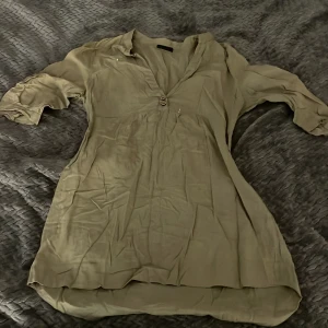 Beige kortklänning från Vero Moda - Snygg beige kortklänning från Vero Moda med v-ringning och två knappar framtill. Klänningen har trekvartsärmar med lätt puff och är tillverkad i ett tunt, luftigt tyg som känns skönt mot huden. Perfekt för en avslappnad och trendig look. Tycker den är väldigt bra som strandklänning❤️