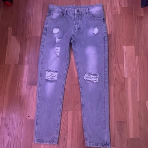 Grå slitna skinny jeans 12Y - Säljer ett par grå skinny jeans med slitningar och hål på benen. Jeansen har klassisk femficksdesign, normal midja och är tillverkade i en mix av bomull och polyester. Perfekta för dig som gillar en edgy och trendig look.