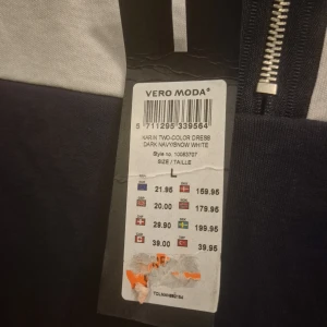 Tvåfärgad klänning från Vero Moda - Mörkblå och vit klänning från Vero Moda i enkel, rak modell. Klänningen har trekvartsärm och en snygg dragkedja bak. Perfekt för dig som gillar stilren design med kontrastfärger. Materialet känns mjukt och bekvämt.