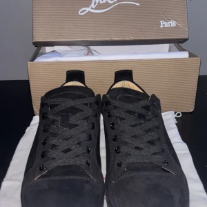 Svarta sneakers från Christian Louboutin 🏆 PRIS KAN DISKUTERAS 🏆  - Snygga svarta sneakers från Christian Louboutin i mocka med klassisk röd sula och diskret logga. Skorna har rund tå, svarta snören och en stilren design som passar perfekt till streetwear eller en mer dressad look.