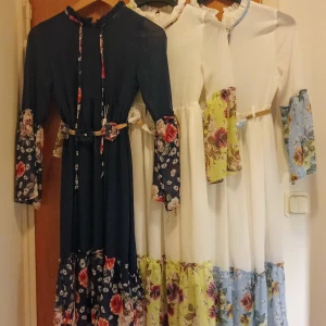 Långklänning med blommiga detaljer - Säljer romantiska långklänningar i marinblått och vitt med blommiga inslag på ärmar och nederkant. Klänningarna har långa ärmar, volangdetaljer och knytband i midjan med matchande blommor. Perfekt för dig som gillar en bohemisk och färgglad stil.        Alla 3= 300:- eller 100:-/st.   Stl är ca 11-13 år