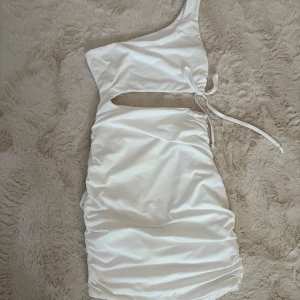 Vit one shoulder klänning från SHEIN - Snygg vit kortklänning från SHEIN med one shoulder-design och cut out-detalj i midjan. Klänningen har knytband på sidan och är tillverkad i mjuk polyester. 