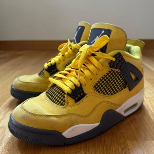 Nike Air Jordan 4 Lightning - Snygga Nike Air Jordan 4 sneakers i gul nubuck  med svarta detaljer och vit mellansula. Skorna har klassisk snörning, meshpaneler och Jumpman-loggan på plös och sula. Fint använt skick.