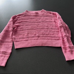 Rosa stickad croppad tröja H&M - Söt rosa stickad tröja från H&M med croppad passform och lång ärm. Tröjan har ett genomgående hålmönster och bred ribbad mudd vid midja och ärmslut. Perfekt för dig som gillar en chill och trendig stil.