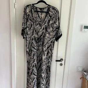 Klänning / Kaftan - Snygg långklänning från Lindex i svartvitt mönster med blad. Klänningen har lös passform, 3/4 ärmar och knyt i midjan. Perfekt för dig som gillar statement-plagg med coolt print och avslappnad stil.