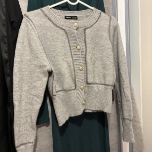 Grå kofta från SHEIN med guldknappar - Superfin grå kofta från SHEIN med snygga guldiga knappar framtill. Koftan är stickad, har lång ärm och ribbade detaljer vid hals, knappslå och midja. Perfekt till lager-på-lager och enkel att styla till olika outfits.