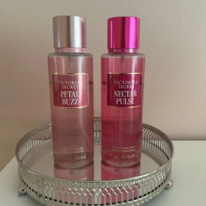 Victoria's Secret Petal Buzz & Nectar Pulse - Två rosa doftmist från Victoria's Secret: Petal Buzz och Nectar Pulse. Båda flaskorna rymmer 250 ml och har eleganta metallicfärgade lock, ett i silver och ett i rosa. Perfekta för dig som gillar fräscha och blommiga dofter med en lyxig känsla.