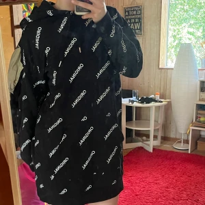 Svart hoodie med vit text och huva - Säljer en svart hoodie med vit text där det står 'ORIGINAL' tryckt över hela tröjan. Hoodien har huva med snörning och långa ärmar. Perfekt för dig som vill ha en hoodie att chilla i.