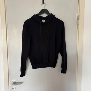 Svart hoodie från H&M Divided XS - En klassisk svart hoodie från H&M Divided i storlek XS. Tröjan har huva med snörning, magficka och ribbade muddar vid ärmslut och nederkant. Perfekt för en chill och avslappnad stil.