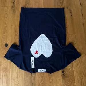 Mörkblå Comme des Garçons Play t-shirt - Snygg mörkblå t-shirt från Comme des Garçons Play med stort vitt hjärta och röd logga med ögon på bröstet. Klassisk passform och korta ärmar, tillverkad i mjuk bomull. Aldrig använd och är i storlek L men passar även dem som har storlek M