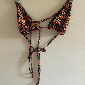 Bikinitopp - Svart bikini topp med blommmönster i orange. Storlek 34 tror jag men inte säker eftersom det inte finns någon lapp. Köpt på stadium. Sparsamt använd💕