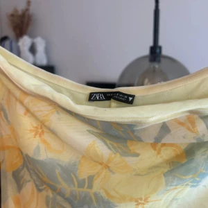 Blommig axelbandslös klänning från Zara - Superfin axelbandslös långklänning från Zara med blommigt mönster i ljusgult och blått. Klänningen har en figurnära passform och är perfekt för sommardagar. Tunt, svalt material som känns luftigt och bekvämt. Defekten som jag la märke till visas på sista bilden. Tyget har alltså gått upp lite , men detta är dock underkjolen som är under yttersta lagret så detta är inget man tänker på när man har på sig klänningen!🤗☺️