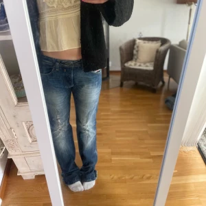 Blå raka jeans från Diesel - Säljer ett par blå jeans från Diesel med slitna detaljer och raka ben. Jeansen har låg midja och klassisk femficksdesign. Materialet är jeans med snygg tvätt och slitningar framtill för en cool, avslappnad look.