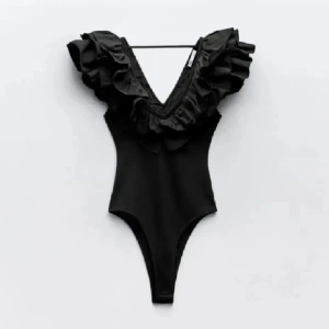 Svart body från Zara - Supersnygg svart bikini från Zara med djup v-ringning och stora volanger runt axlar och hals. Modellen är stilren och ger en riktigt trendig look. Perfekt för dig som vill sticka ut på stranden eller vid poolen. Materialet känns mjukt och följsamt.