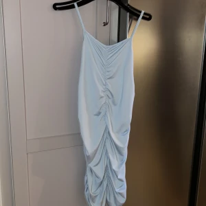 Ljusblå satin klänning med rynk - Supersöt ljusblå kortklänning i satin med smala axelband och snygg rynkdetalj framtill. Materialet är väldigt stretchigt så den anpassar sig efter din kroppsform