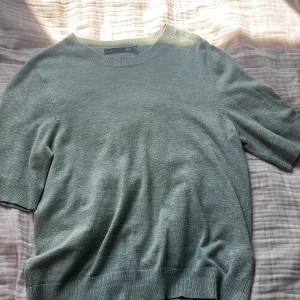 Grå stickad kortärmad tröja - En stilren grå stickad tröja från lager 157 med korta ärmar och rund hals. Tröjan har ribbade muddar vid ärmslut och nederkant, vilket ger en clean och enkel look. Perfekt för lager-på-lager eller som den är under vår och sommar.