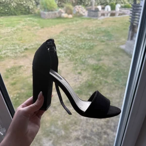 Klackar från Nelly✨ - Stilrena svarta klackar med hög blockklack och öppen tå från Nelly. Skorna har en bred rem över tårna och justerbart spänne vid ankeln. Ytan är i mockaliknande material som ger en lyxig känsla. Perfekta för dig som vill ha en clean och trendig look. Använda en gång på studentbal✨