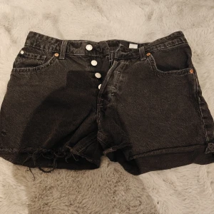 Svarta 90's boyfriend jeansshorts från H&M - Svarta 90's boyfriend shorts från H&M i denim med låg midja. De har en avslappnad passform, knappar framtill och råa, fransiga benslut för en cool vintagekänsla. Perfekta för dig som gillar en chill och trendig stil.