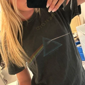 Pink Floyd Dark Side of the Moon t-shirt - Svart t-shirt med ikoniskt Dark Side of the Moon-tryck från Pink Floyd på framsidan och turnédatum från 1973 på ryggen. Klassisk passform med korta ärmar och rund hals. Perfekt för dig som älskar vintageband-merch och vill sticka ut med en tidlös rockstil.