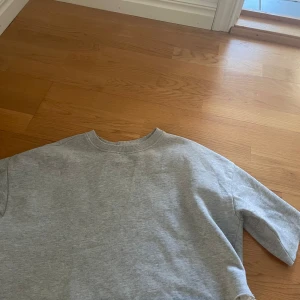 Grå sweatshirt i bomull - En basic grå sweatshirt med rund halsringning och korta ärmar. Tröjan är i mjuk bomull och har en avslappnad passform, perfekt för chill dagar eller när du vill ha en enkel och stilren look.